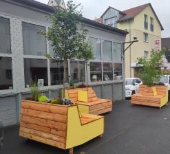 Bank aus Holz mit einem Baum in der Mitte und Pflanzkästen